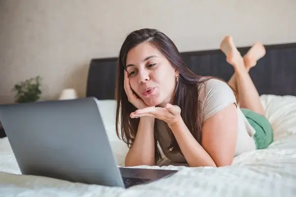 Kvinna flörtar under sexchatt på laptop, liggande på säng, online sexdate och sex contact site kommunikation
