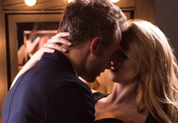 Man i kostymjacka som är på väg att kyssa en kvinna med blont hår och rött läppstift i en sensuell, intim pose, vilket antyder ett romantiskt eller sexuellt möte.