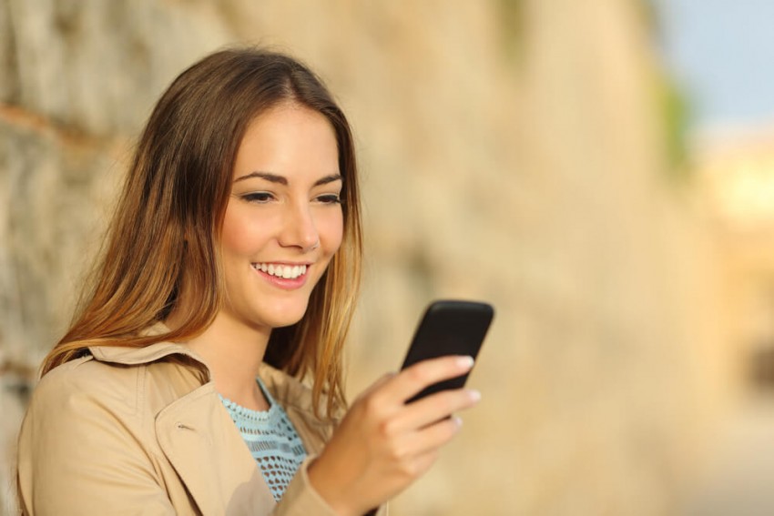 Kvinna i svart spetsunderkläder tar selfie i sängen, symboliserar videotelefonsex och intim chatt.