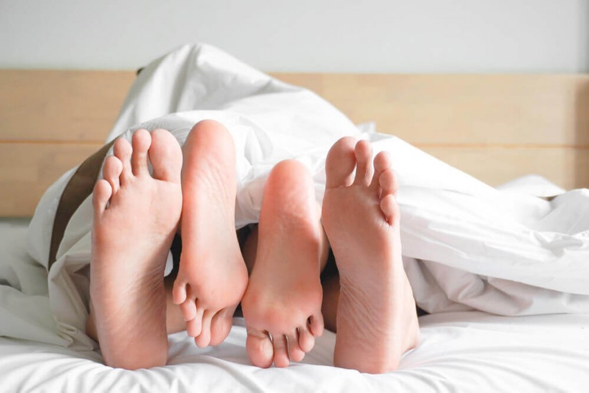 Vuxen dejting som leder till sex ikväll, två personers bara fötter under ett vitt täcke i en säng.